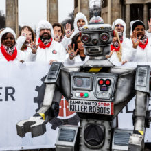 Robottiaseiden vastaisen kampanjan tempaus, etualalla robotti ja takana valkoisiin haalareihin pukeutuneita ihmisiä